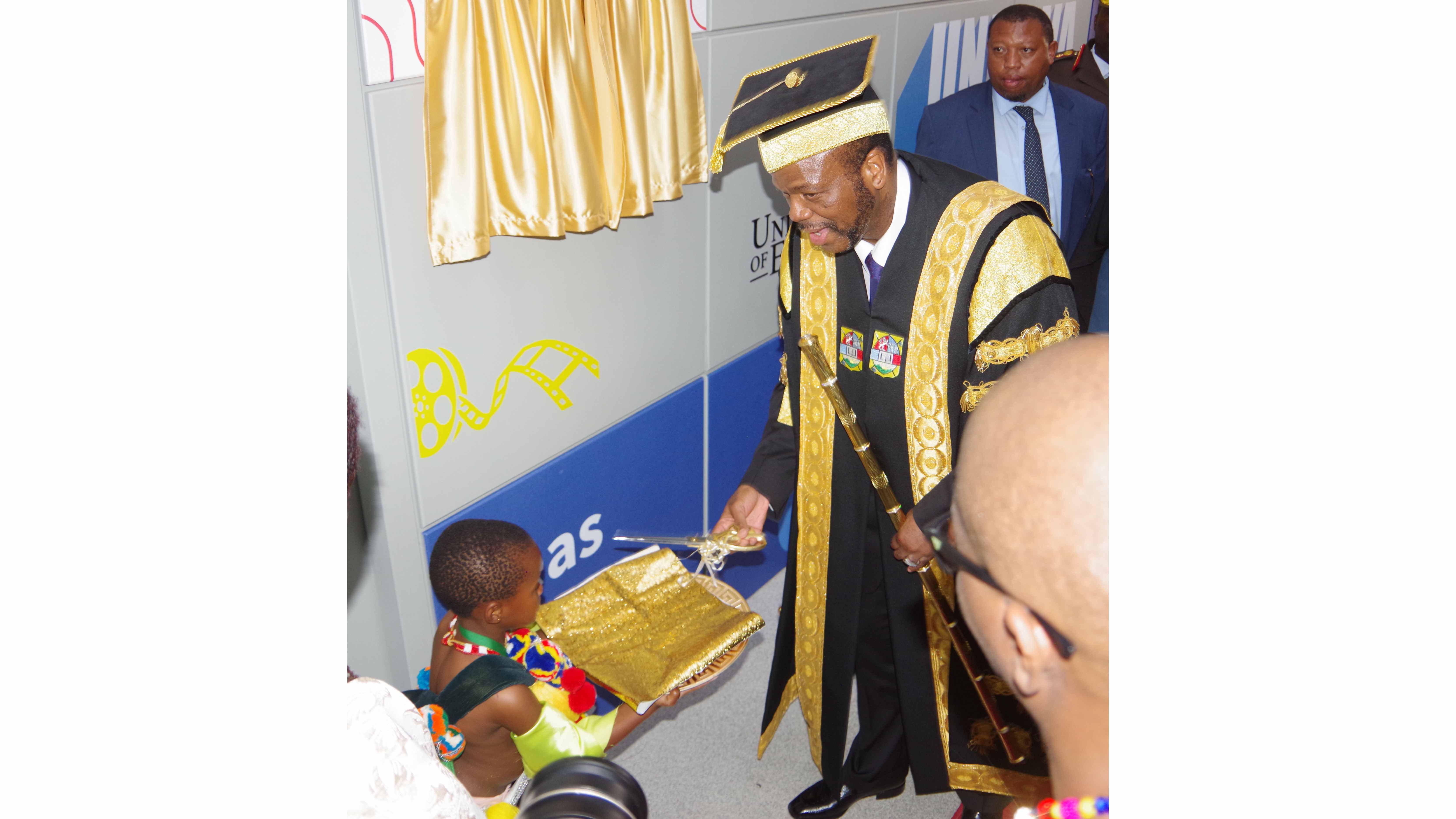 His Majesty King Mswati III takes a pair of scissors from Ayabonga Dlamini before cutting the ribbon at the UNESWA Content Development Lab. 